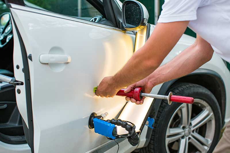 A technician uses paintless dent repair tools on a car door
